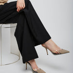 Person wearing black pants and beige high-heeled shoes sitting on a chair against a plain background