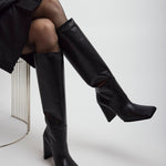 Person wearing black knee-high boots on a white background