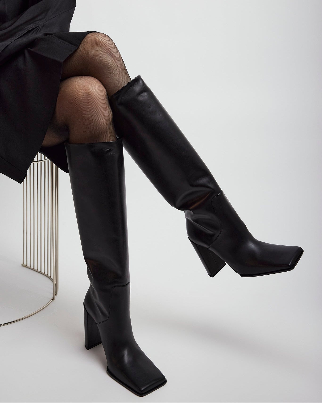 Person wearing black knee-high boots on a white background
