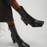 Black ankle boots worn with a black skirt on a light gray background