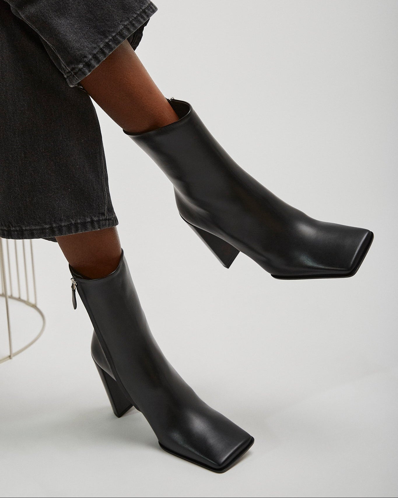 Black ankle boots worn with a black skirt on a light gray background
