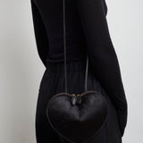 Person wearing a black heart-shaped bag on a plain background