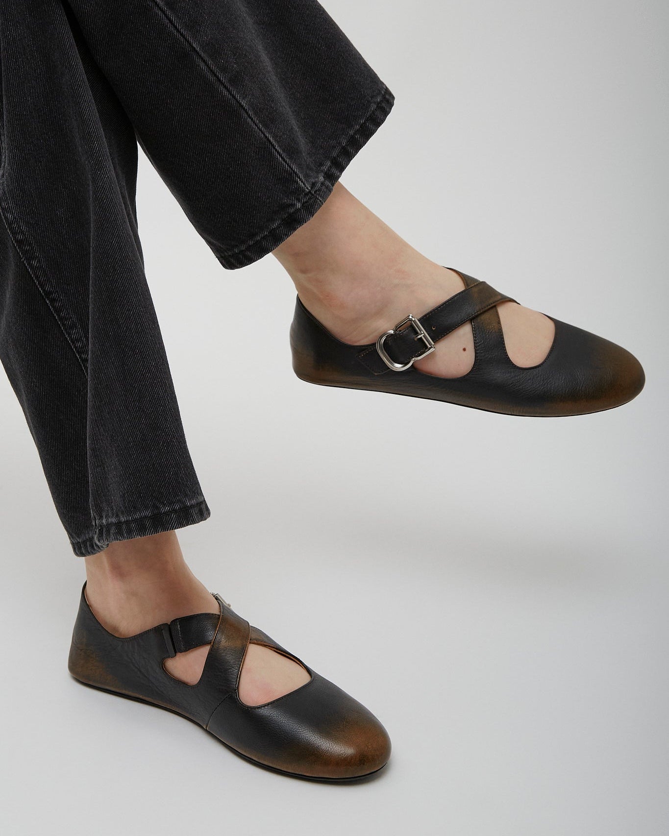 Black leather sandals worn with black pants on a light gray background