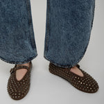 Brown studded flats worn with blue jeans on a plain background