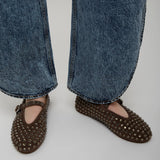 Brown studded flats worn with blue jeans on a plain background