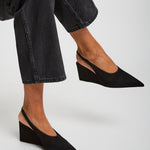 Person wearing black wedge shoes and black jeans on a light gray background
