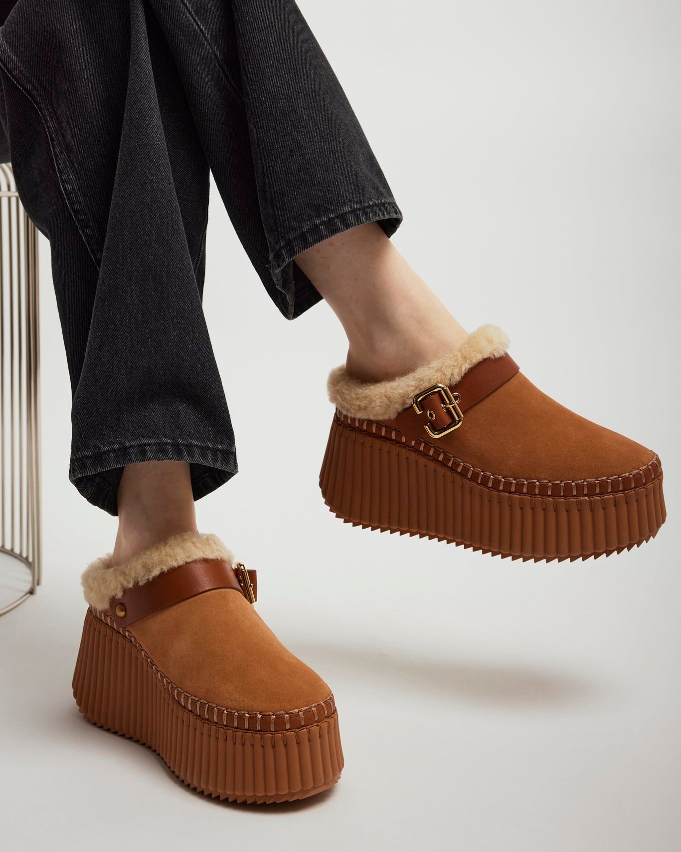 Brown platform shoes with fur trim worn by a person sitting on a chair.