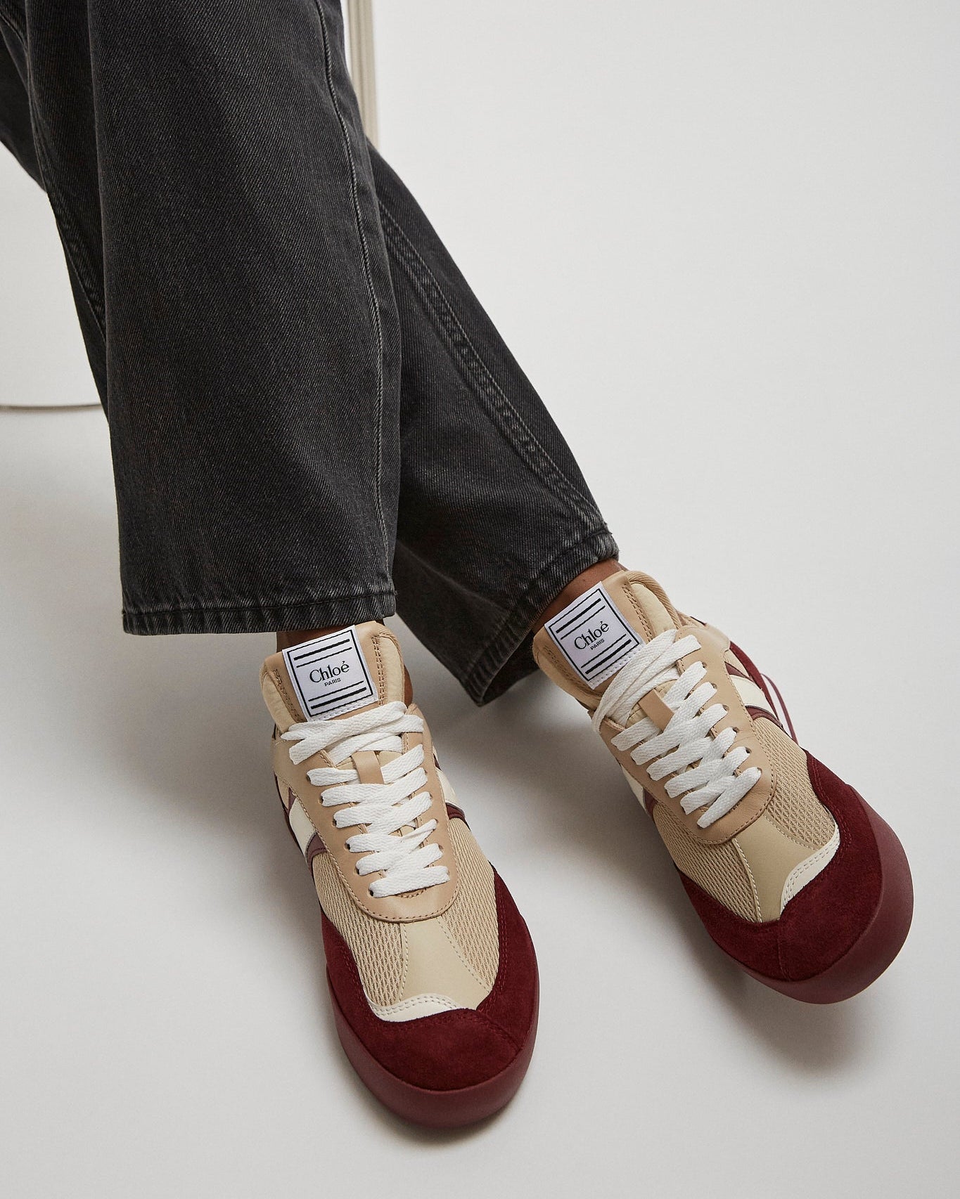 Beige and burgundy sneakers worn with black jeans on a white background
