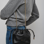 Person wearing a gray sweater with a black handbag featuring a gold chain strap on a plain background