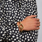 Person wearing a black and white polka dot dress with a gold bracelet on a plain background