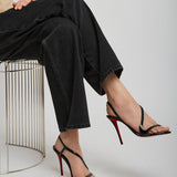 Person wearing black high-heeled sandals sitting on a white stool against a plain background