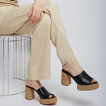 Person wearing black platform sandals with cork soles on a white background