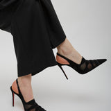 Black high-heeled shoes worn with black pants on a light gray background