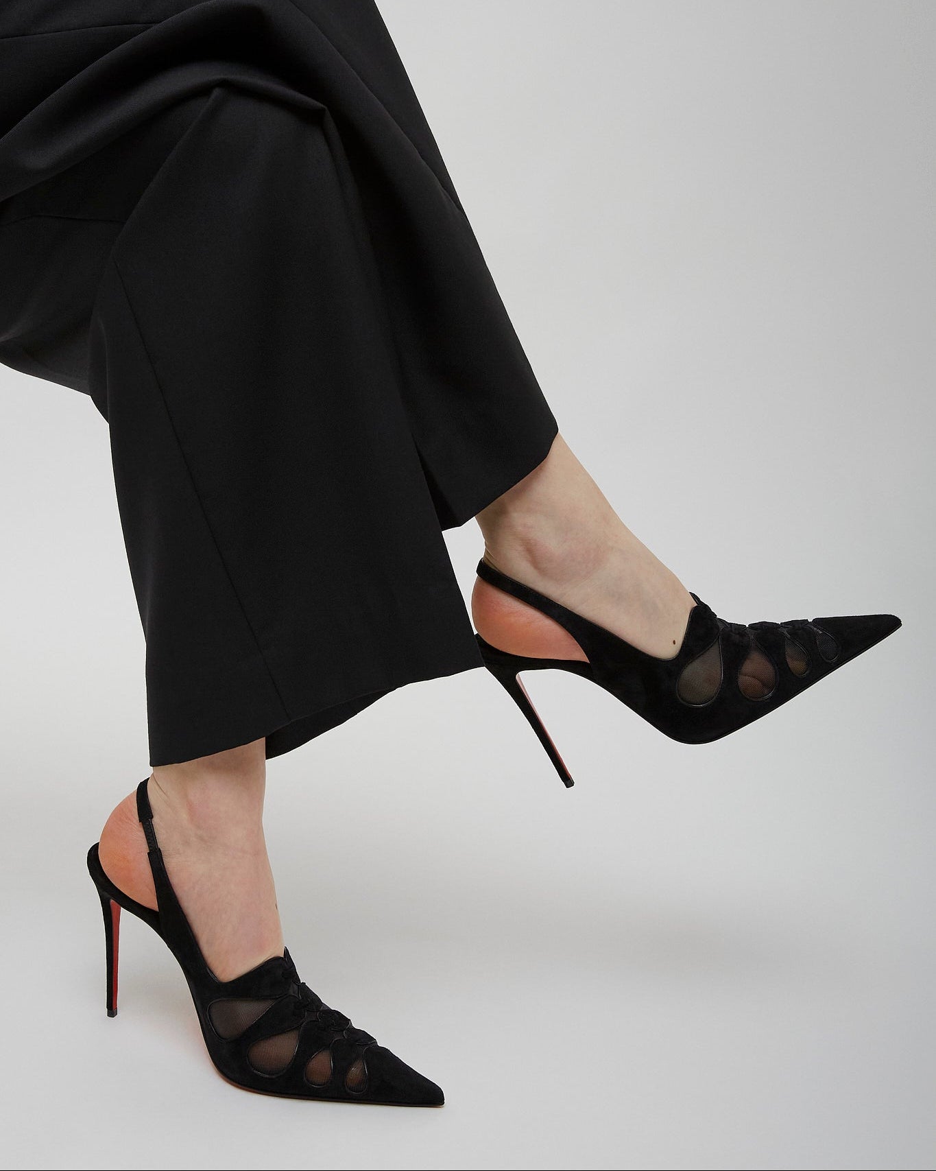 Black high-heeled shoes worn with black pants on a light gray background