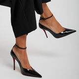 Black high-heeled shoes with red soles worn by a person in black pants on a light gray background
