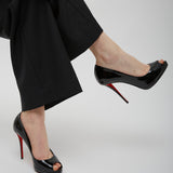 Black high-heeled shoes with red soles worn by a person in black pants on a light gray background