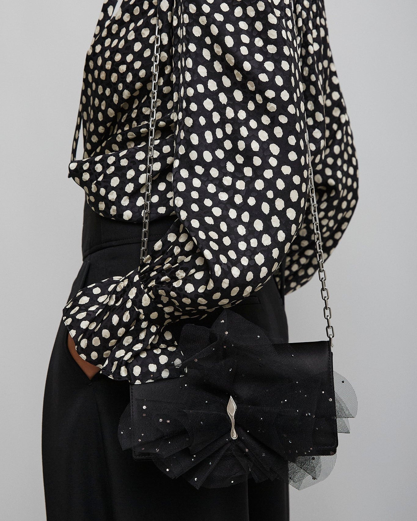 Person wearing a black and white polka dot blouse with a black handbag on a gray background