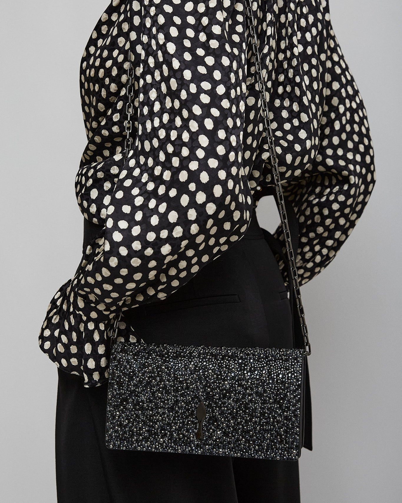 Person wearing a black and white polka dot blouse with a black skirt and black clutch bag on a gray background