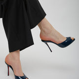 Navy high-heeled shoes worn with black pants on a light gray background