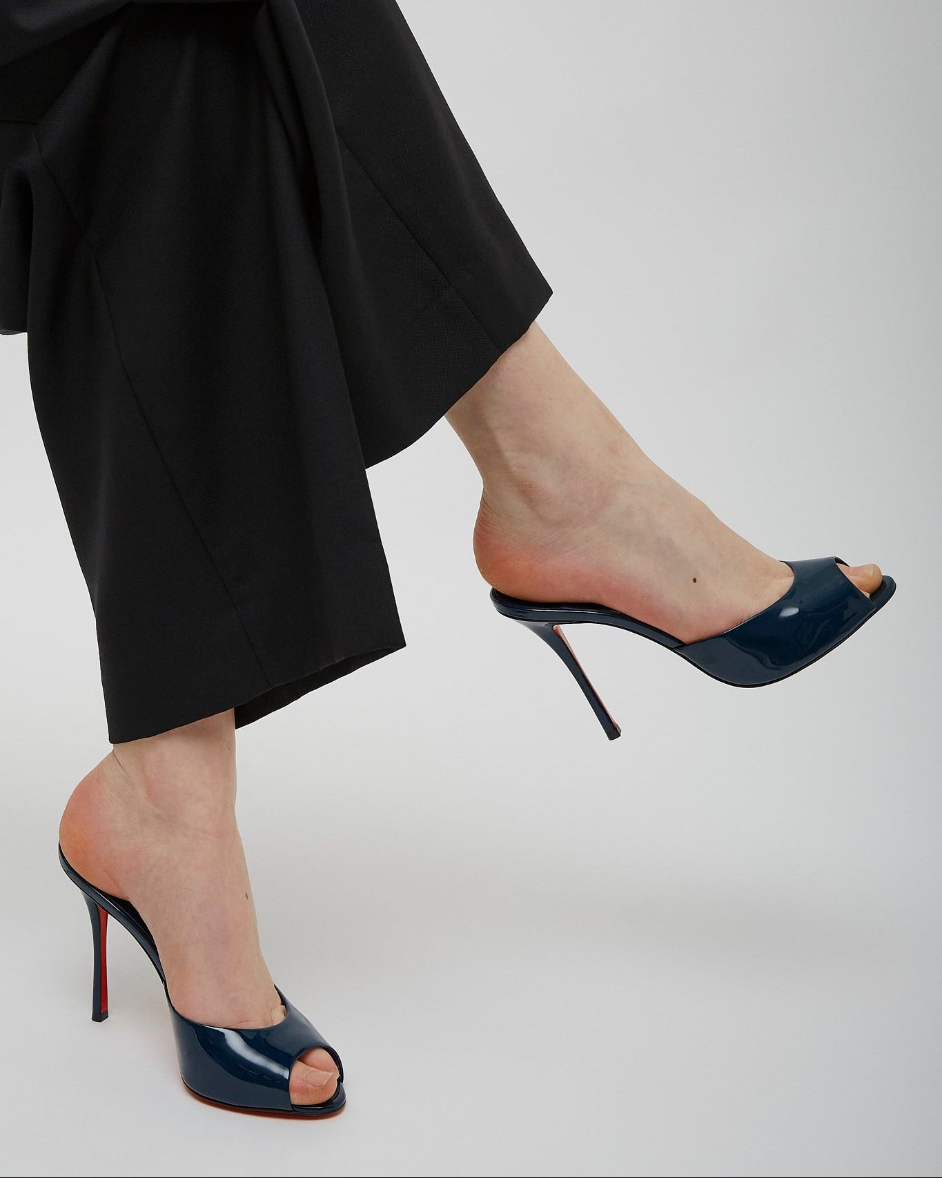 Navy high-heeled shoes worn with black pants on a light gray background