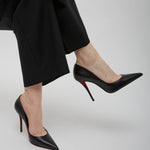 Person wearing black high-heeled shoes with red soles and black pants on a light gray background