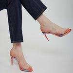 Person wearing blue jeans and colorful high-heeled shoes on a plain background