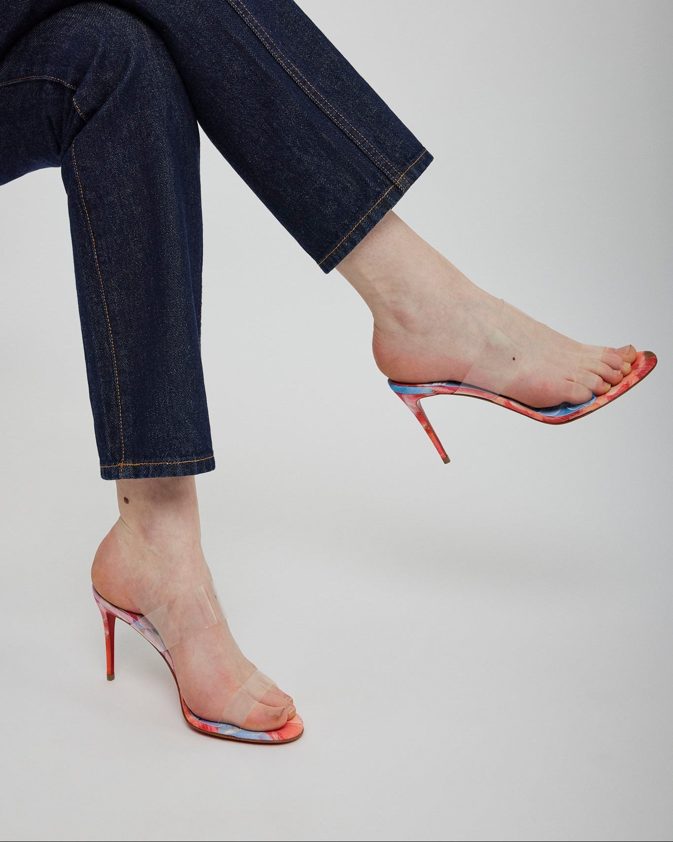 Person wearing blue jeans and colorful high-heeled shoes on a plain background