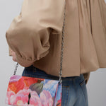 Person wearing a beige jacket with a colorful floral handbag on a plain background