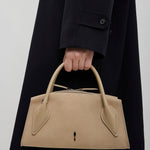 Person holding a beige handbag with a plain background