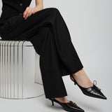 Person wearing a black outfit with high-waisted pants and black shoes on a white background