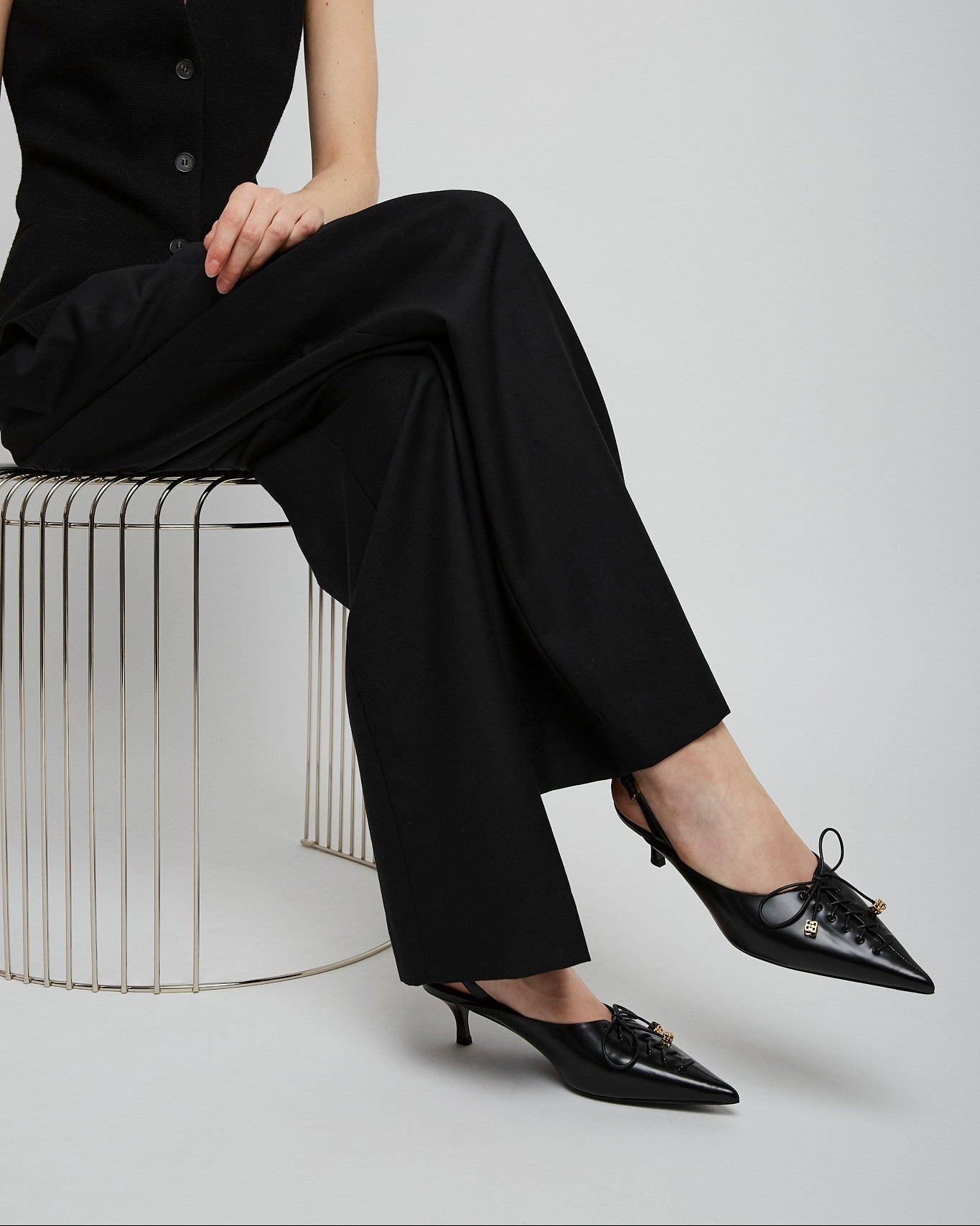 Person wearing a black outfit with high-waisted pants and black shoes on a white background