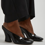 Black high-heeled shoes worn with a black outfit on a light gray background