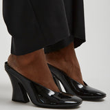 Black high-heeled shoes worn with a black outfit on a light gray background