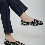 Black flats with silver embellishments worn with blue jeans on a light gray background