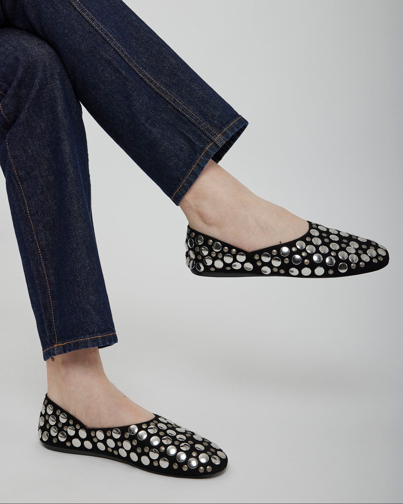 Black flats with silver embellishments worn with blue jeans on a light gray background
