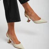 White high-heeled shoes worn with black jeans on a light gray background