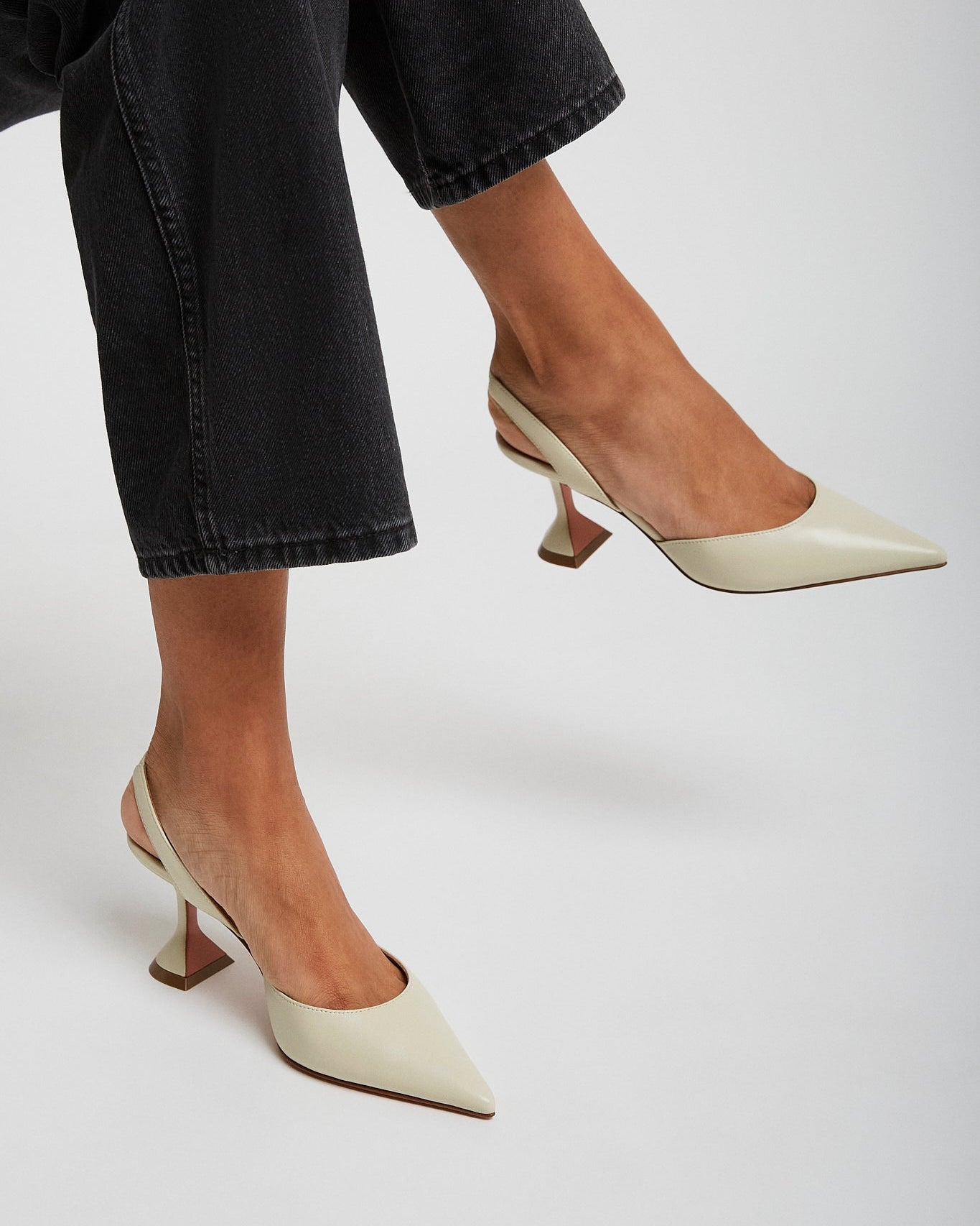 White high-heeled shoes worn with black jeans on a light gray background