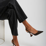 Person wearing black high-heeled shoes and dark pants sitting on a white background