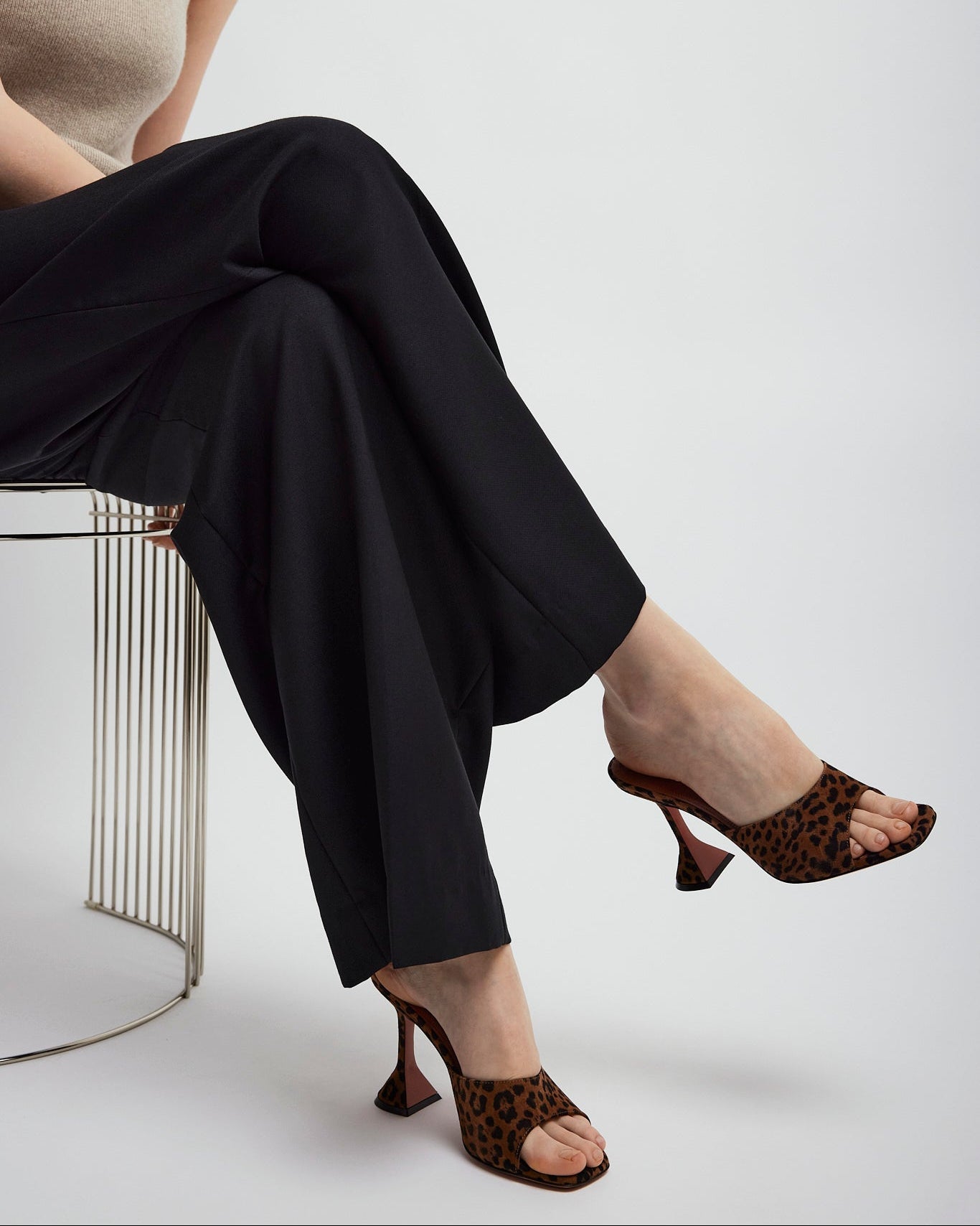 Person wearing black pants and leopard print high heels on a white background