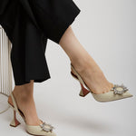 Person wearing black pants and beige high-heeled shoes with decorative elements on a white background