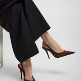 Person wearing leopard print high heels and black pants on a light gray background
