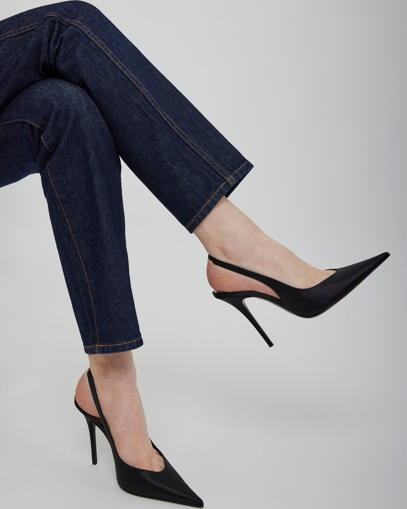 Black high-heeled shoes worn with blue jeans on a light gray background