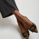 Leopard print shoes with black buckles worn by a person in a casual outfit.