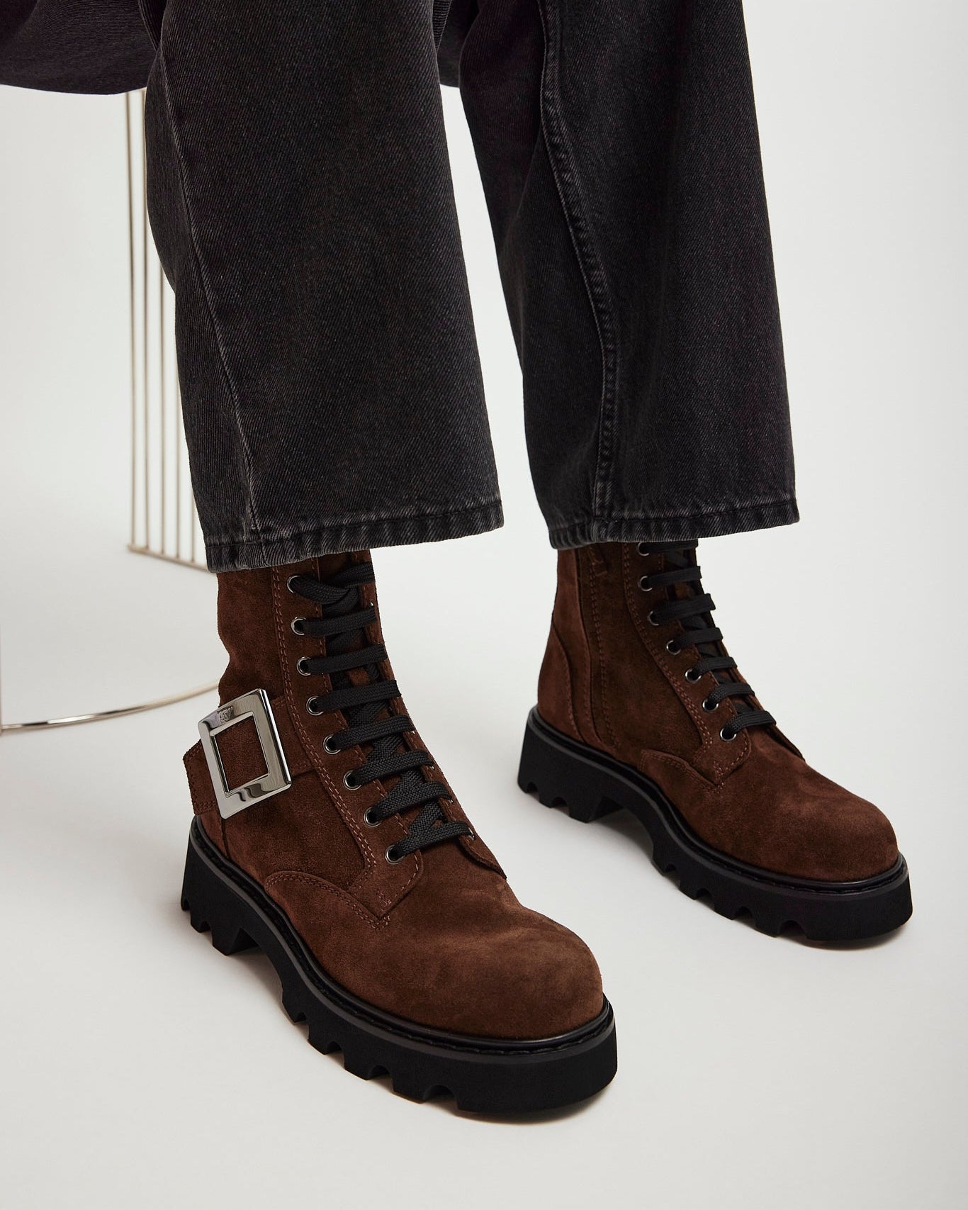 Brown suede boots with black soles worn with dark jeans on a white background