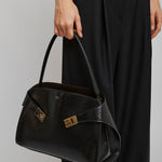 Person holding a black handbag with gold accents on a plain background