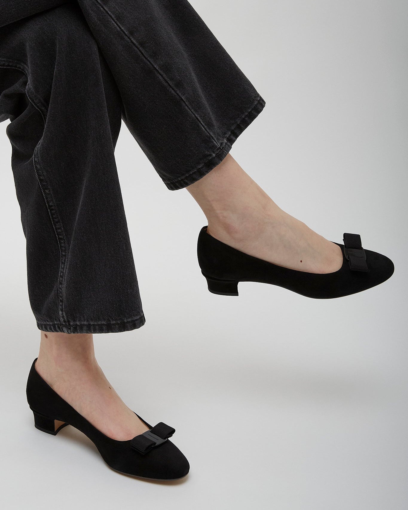 Person wearing black shoes with bows and black pants on a light gray background
