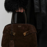 Brown textured handbag with gold accents held by a person wearing a black coat.