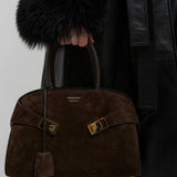 Brown textured handbag with gold accents held by a person wearing a black coat.