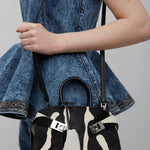 Person holding a black and white patterned handbag with a denim jacket.