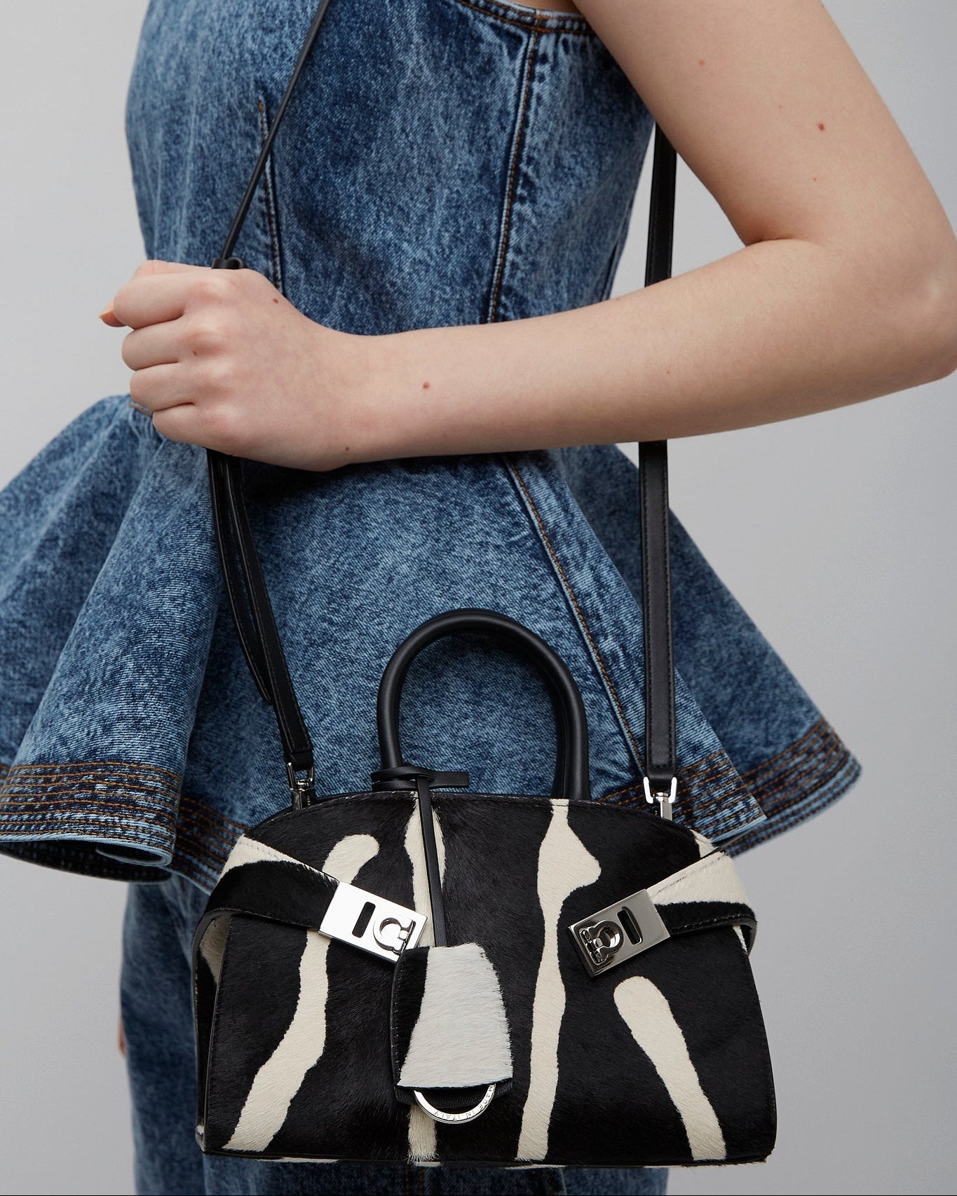 Person holding a black and white patterned handbag with a denim jacket.